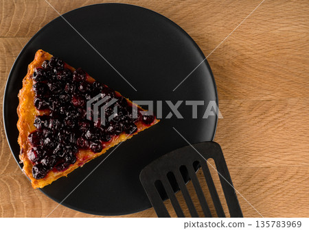 Pie with carrots and currants sprinkled on top on a black plate and cutlery a spatula for frying, partly present in the frame on a wooden board Pie with carrots and currants sprinkled on top on a black plate and cutlery a spatula for frying, partly present in the frame on a wooden board 135783969