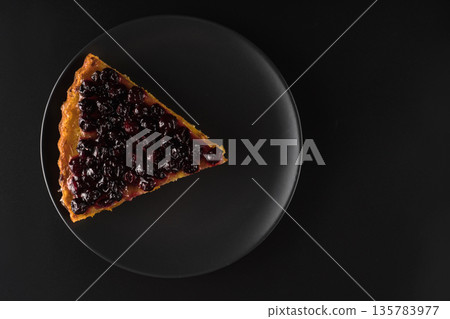 Sliced piece of carrot pie from above thickly covered with currant berries, charlotte on a black plate on a black background on a wooden board 135783977
