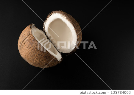 One ripe coconut divided into two parts, on a black background, isolated One ripe coconut divided into two parts, on a black background, isolated 135784003