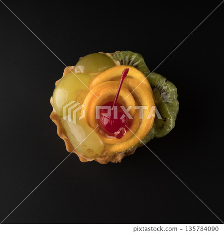 Fruit dessert cake with cherries, grapes sponges, kiwi slices and orange slices on a black background isolated Fruit dessert cake with cherries, grapes sponges, kiwi slices and orange slices on a black background isolated 135784090