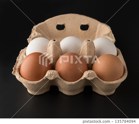 Chicken eggs, in the amount of six pieces in a disposable paper tray on a black background, isolated Chicken eggs, in the amount of six pieces in a disposable paper tray on a black background, isolated 135784094