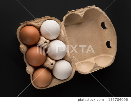 Chicken eggs, in the amount of six pieces in a disposable paper tray on a black background, isolated 135784096