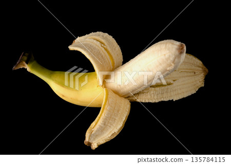 One ripe banana, half peeled, on a black background, isolated One ripe banana, half peeled, on a black background, isolated 135784115
