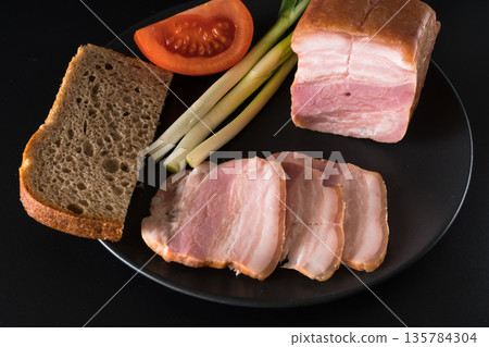Food, lard, green onions, tomato, black bread, on a black plate on a black background Food, lard, green onions, tomato, black bread, on a black plate on a black background 135784304