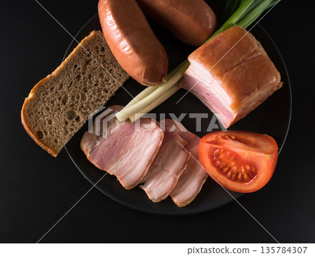 Food, lard, green onions, tomato, black bread, sausages, on a black plate on a black background 135784307