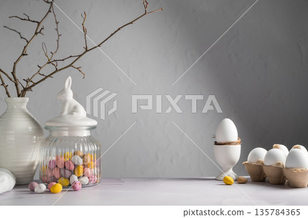 Easter background with mini egg candies in a jar, twigs in a vase and white chicken eggs 135784365