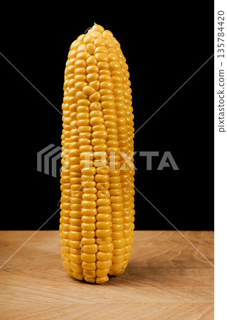 One swing of young peeled corn on a wooden board on a black background close-up 135784420