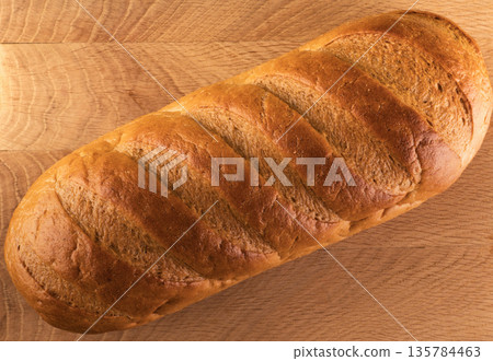 A whole loaf of bread on a wooden board, view from the top A whole loaf of bread on a wooden board, view from the top 135784463