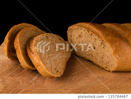 part of a loaf of bread and slices cut from it, laid on a wooden board, on a black background part of a loaf of bread and slices cut from it, laid on a wooden board, on a black background 135784467