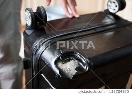 Damaged black suitcase with broken corner after rough baggage handling at airport 135784550