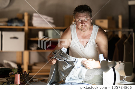 Middle-aged male dressmaker reviewing jeans to restore 135784866