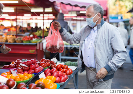 Middle aged man in mask buying vegetables 135784880
