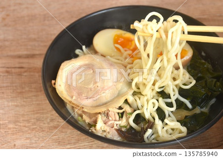 chopsticks picking Tonkotsu Chashu ramen orJapanese yellow noodles topping slice braised pork with boiled egg and seaweed in Miso soy sauce on bowl 135785940