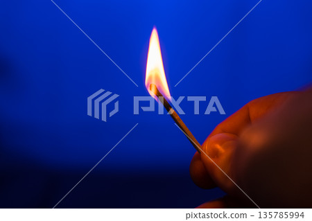 Burning match in right hand on blue background Burning match in right hand on blue background 135785994