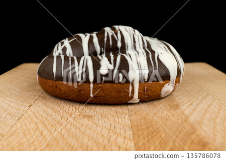 bun covered with chocolate, on a wooden board on a black background bun covered with chocolate, on a wooden board on a black background 135786078