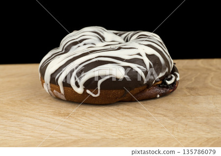 bun covered with chocolate, on a wooden board, on a black background bun covered with chocolate, on a wooden board, on a black background 135786079