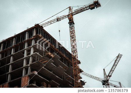 Urban construction of a high-rise building with tower cranes against an overcast sky. Modern architecture, industry, urban growth themes. Real estate. Urban construction of a high-rise building with tower cranes against an overcast sky. Modern architecture, industry, urban growth themes. Real estate. 135786379