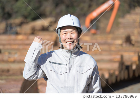 A Japanese woman wearing a helmet and pumping her fist at a construction site A Japanese woman wearing a helmet and pumping her fist at a construction site 135786969