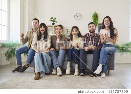 Excited friends cheering while watching a football match on TV together at home Excited friends cheering while watching a football match on TV together at home 135787209