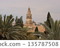 A tall tower with a clock on top stands in front of a lush green forest 135787508