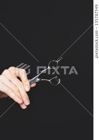 Hand of hairdresser or hairstylist holding professional shears isolated on black background Hand of hairdresser or hairstylist holding professional shears isolated on black background 135787549