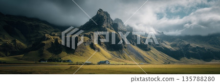Icelandic valley with impressive green mountains and dramatic sky. Lush green Icelandic valley with rugged mountains under a cloudy sky 135788280