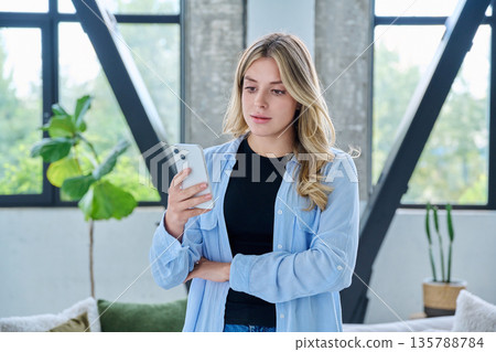 Young woman standing at home using smartphone 135788784