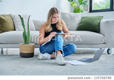 Young female student sitting at home on floor with laptop, notebook, textbook Young female student sitting at home on floor with laptop, notebook, textbook 135788799