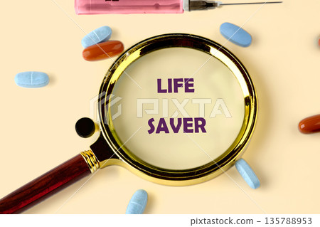 A magnifying glass focuses on the words LIFE SAVER surrounded by various pills and a syringe, emphasizing the importance of medicine and healthcare A magnifying glass focuses on the words LIFE SAVER surrounded by various pills and a syringe, emphasizing the importance of medicine and healthcare 135788953