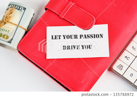 A stack of cash, a calculator, and a card displaying the message LET YOUR PASSION DRIVE YOU rest on a red notebook, suggesting financial planning and ambition A stack of cash, a calculator, and a card displaying the message LET YOUR PASSION DRIVE YOU rest on a red notebook, suggesting financial planning and ambition 135788972
