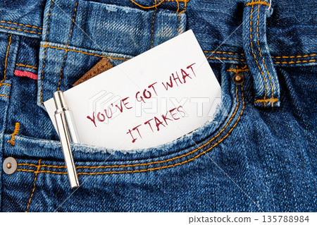 Close up shows blue denim jeans pocket with a white paper note sticking out, with a handwritten message saying you ve got what it takes. A silver pen is also in the pocket 135788984