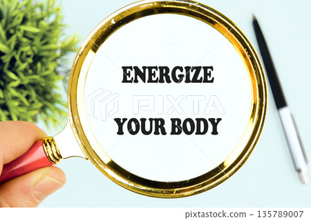 A human hand gently holds a golden magnifying glass, bringing into sharp focus the powerful words energize your body A human hand gently holds a golden magnifying glass, bringing into sharp focus the powerful words energize your body 135789007