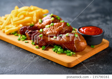 Grilled chicken drumsticks with ketchup and french fry on a black table. Grilled chicken drumsticks with ketchup and french fry on a black table. 135790161