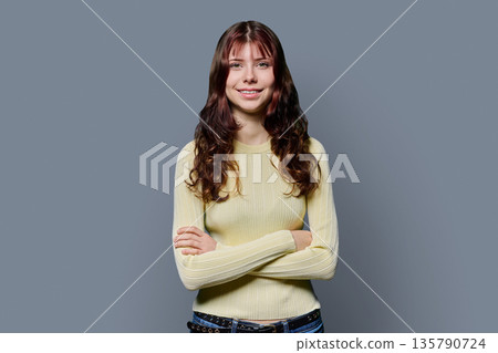 Portrait of smiling confident teenage girl with crossed arms on gray background 135790724