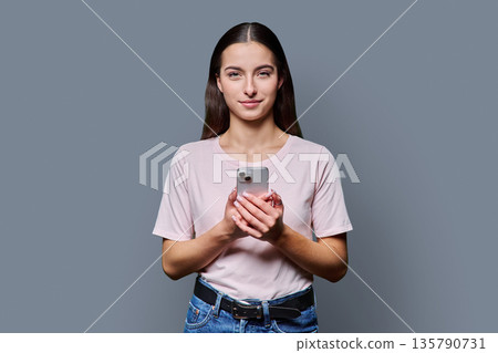 Portrait of smiling teenage girl holding smartphone on gray studio background 135790731