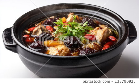 Herbal chicken soup simmers in a black clay pot for wellness 135790923