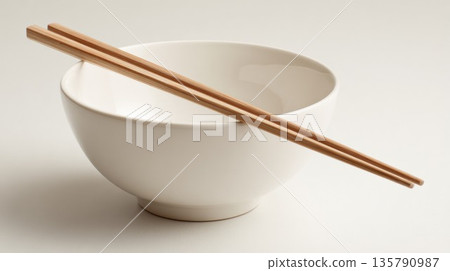Wooden chopsticks resting on a white ceramic bowl 135790987