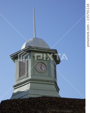 The exterior of a retro clock tower with a steeple soaring into the blue sky. A scene of an old building entangled with withered ivy and a vintage clock face. The exterior of a retro clock tower with a steeple soaring into the blue sky. A scene of an old building entangled with withered ivy and a vintage clock face. 135791116