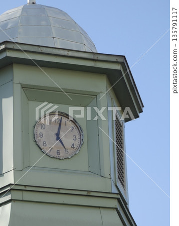 A retro and nostalgic green clock tower that stands out against the blue sky, with an old-fashioned dial and a hand pointing to 5 o'clock that exudes a vintage feel. A retro and nostalgic green clock tower that stands out against the blue sky, with an old-fashioned dial and a hand pointing to 5 o'clock that exudes a vintage feel. 135791117