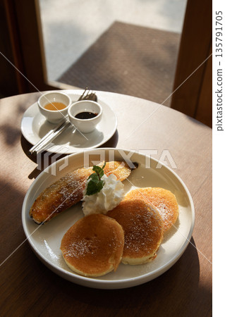 Delicious pancakes with banana and whipped cream in coffee shop or hotel setting under warm natural sunlight in the morning at summer weekend Delicious pancakes with banana and whipped cream in coffee shop or hotel setting under warm natural sunlight in the morning at summer weekend 135791705