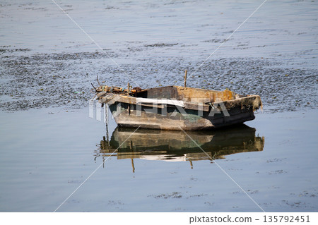 lonely fishing boat docked in calm lake. wooden fishing boat in a still lake water. image of wooden fishing boat moored on the shore. space for text. lonely fishing boat docked in calm lake. wooden fishing boat in a still lake water. image of wooden fishing boat moored on the shore. space for text. 135792451