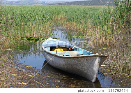 lonely fishing boat docked in calm lake. wooden fishing boat in a still lake water. image of wooden fishing boat moored on the shore. space for text. lonely fishing boat docked in calm lake. wooden fishing boat in a still lake water. image of wooden fishing boat moored on the shore. space for text. 135792454
