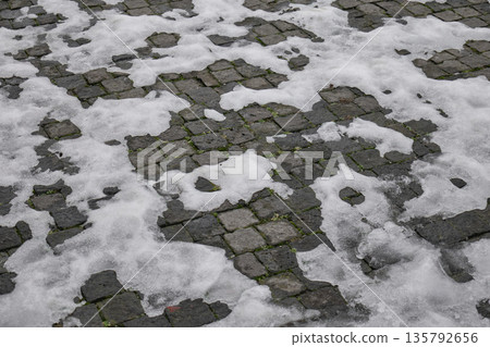 High angle view of patches of white melting snow on textured stone street tiles High angle view of patches of white melting snow on textured stone street tiles 135792656