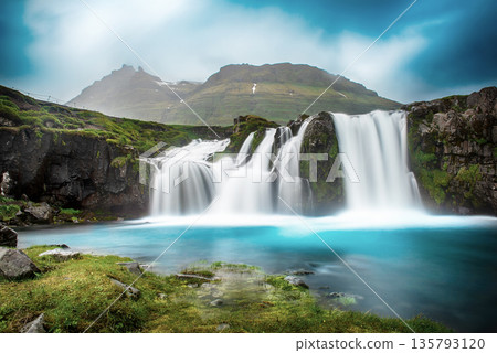 View to the Kirkjufell waterfall at summer. Kirkjufellsfoss waterfall, Iceland, Europe. View to the Kirkjufell waterfall at summer. Kirkjufellsfoss waterfall, Iceland, Europe. 135793120