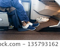 Inflight business class passenger with ample leg room replaces shoes with disposable slippers during flight for comfort travel 135793162