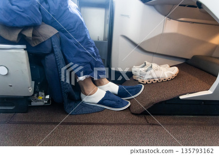 Inflight business class passenger with ample leg room replaces shoes with disposable slippers during flight for comfort travel 135793162
