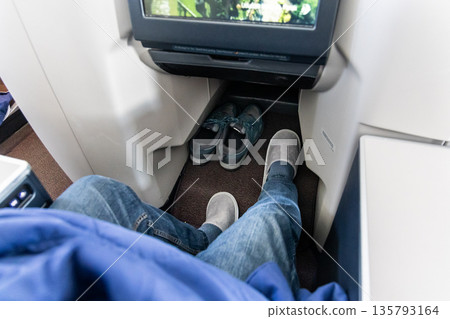 Inflight business class passenger with ample leg room replaces shoes with disposable slippers during flight for comfort travel 135793164