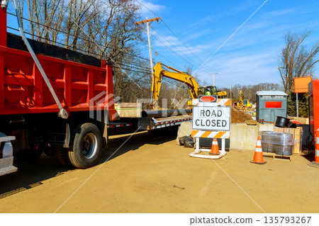 Workers manage construction on road with large machines, barriers during rural location. Workers manage construction on road with large machines, barriers during rural location. 135793267