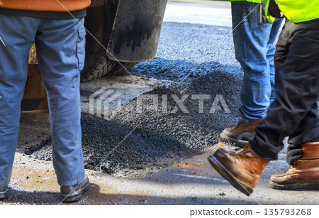 Workers handle asphalt material on road as they prepare for paving work during road repair, Workers handle asphalt material on road as they prepare for paving work during road repair, 135793268