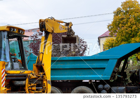 Construction machine uses its arm to load gravel into truck on worksite in city 135793273